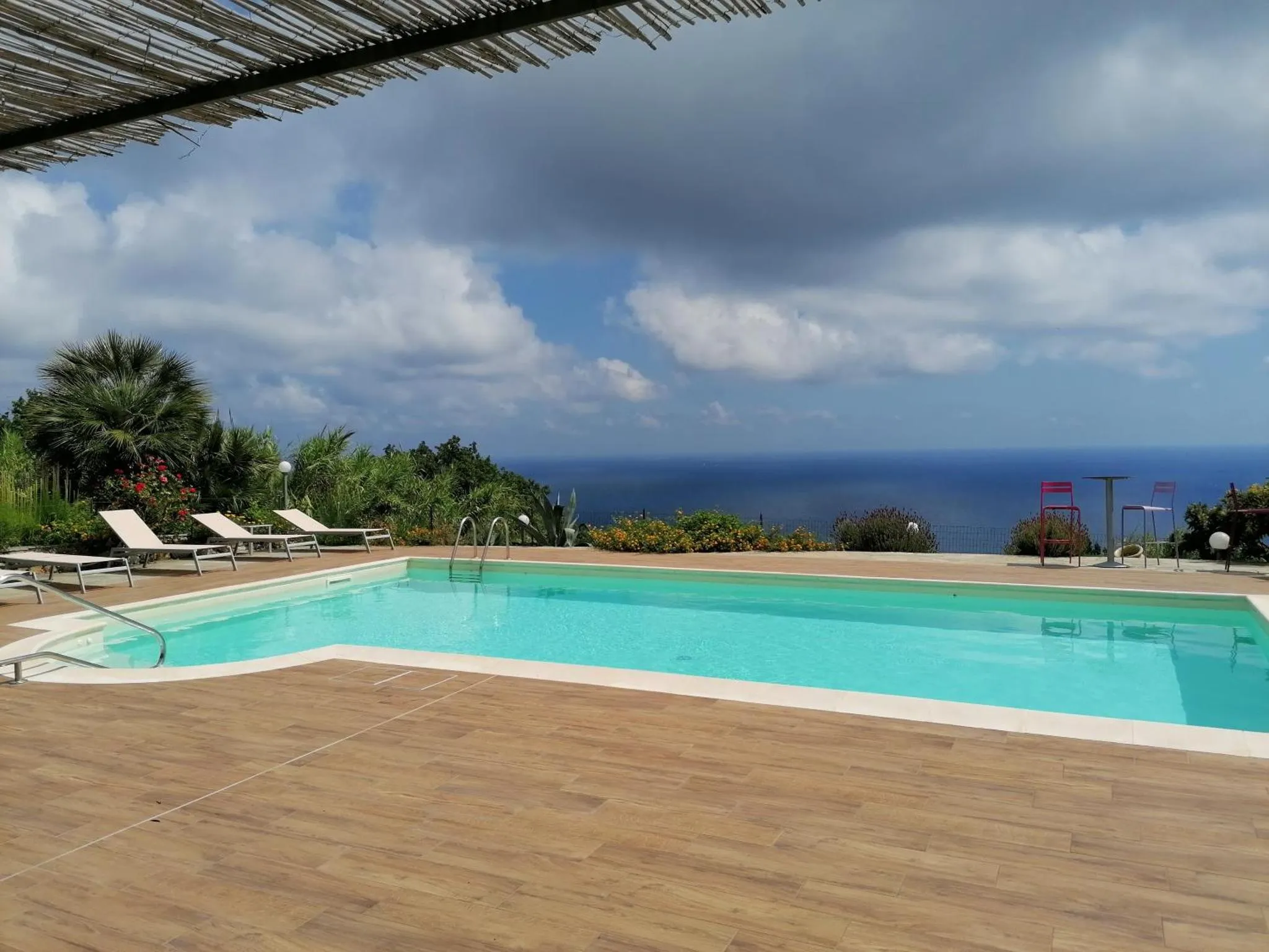Une piscine turquoise avec des transats sur une terrasse en bois, surplombant un paysage marin.