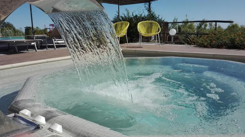 Un jacuzzi extérieur avec une cascade d'eau et des chaises longues colorées.