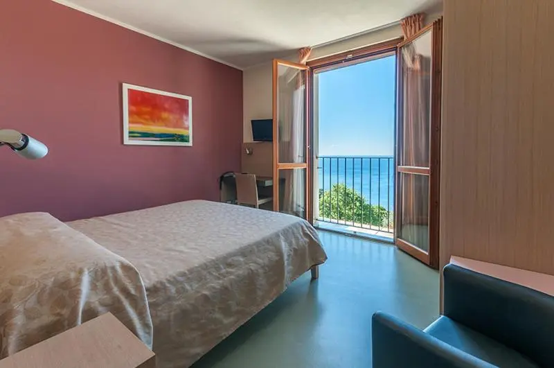 Une chambre lumineuse s'ouvre sur un balcon avec vue sur la mer.
