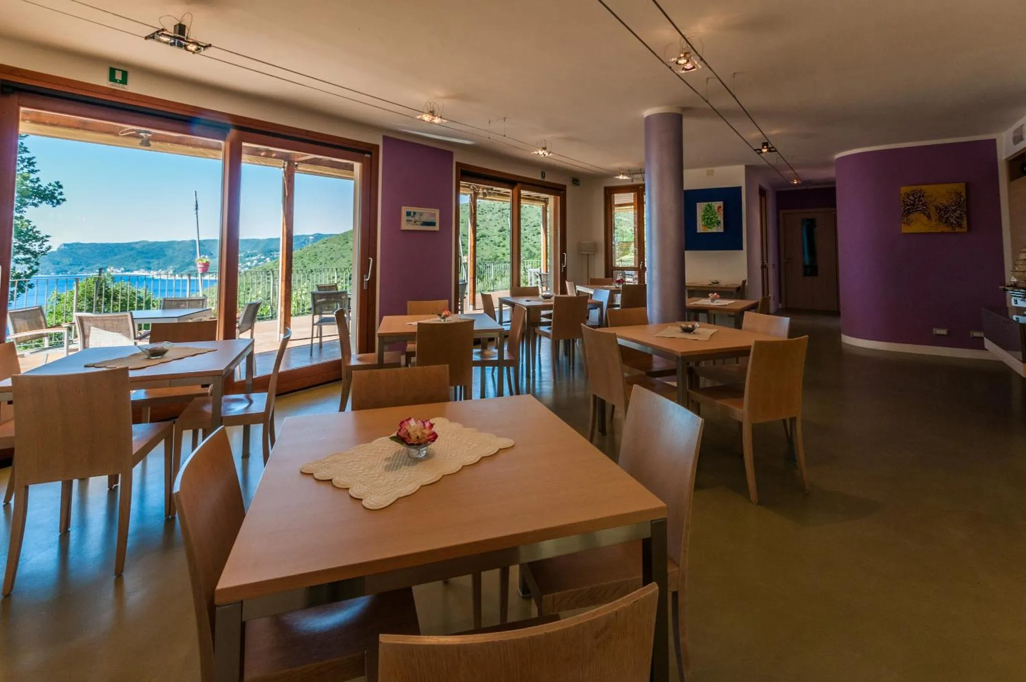 Une salle lumineuse avec des tables et des chaises près de grandes baies vitrées donnant sur un paysage verdoyant.