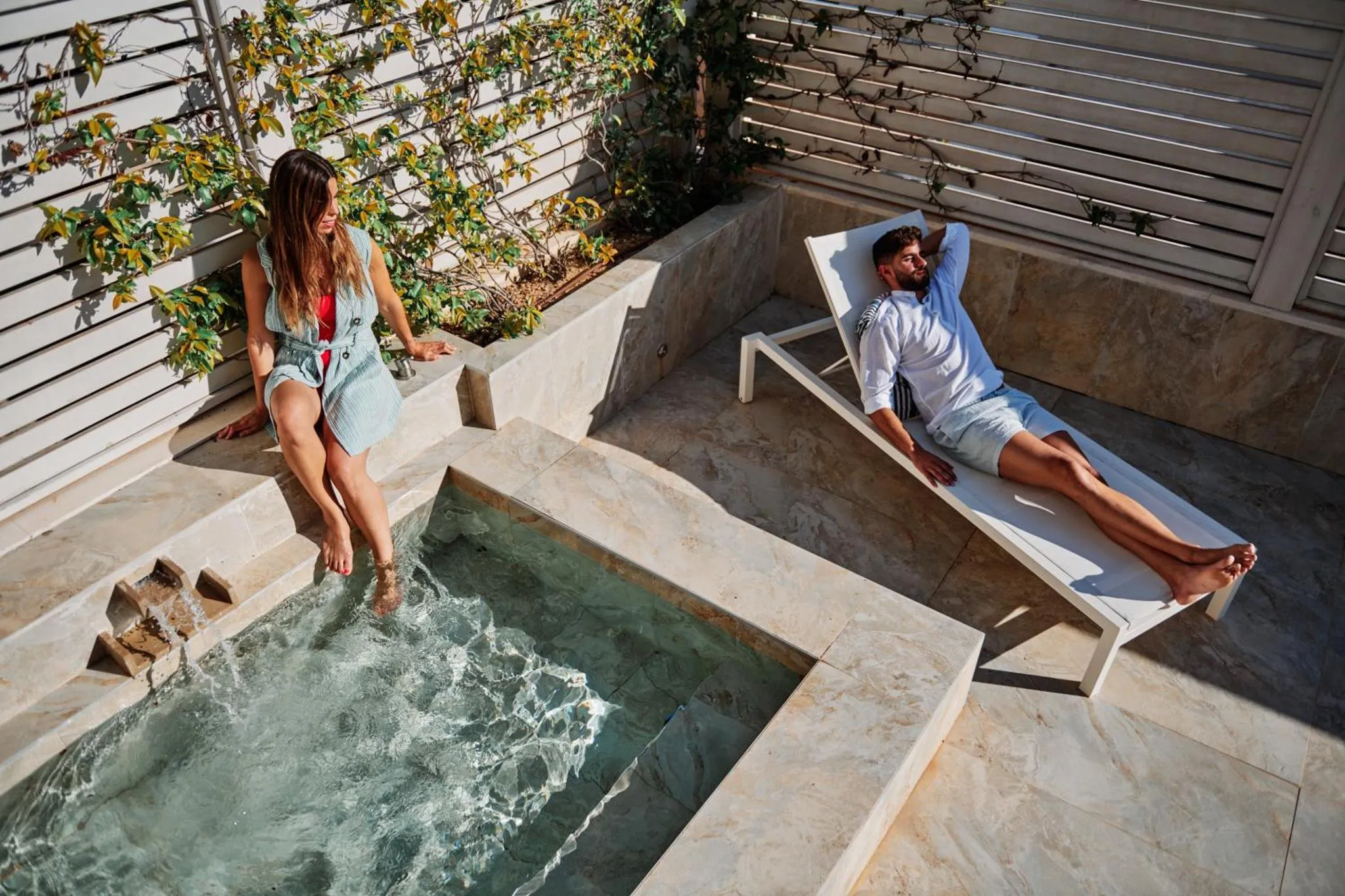 Deux personnes se détendent au bord d'un jacuzzi sur une terrasse ensoleillée.