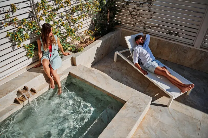 Deux personnes se détendent au bord d'un jacuzzi sur une terrasse ensoleillée.
