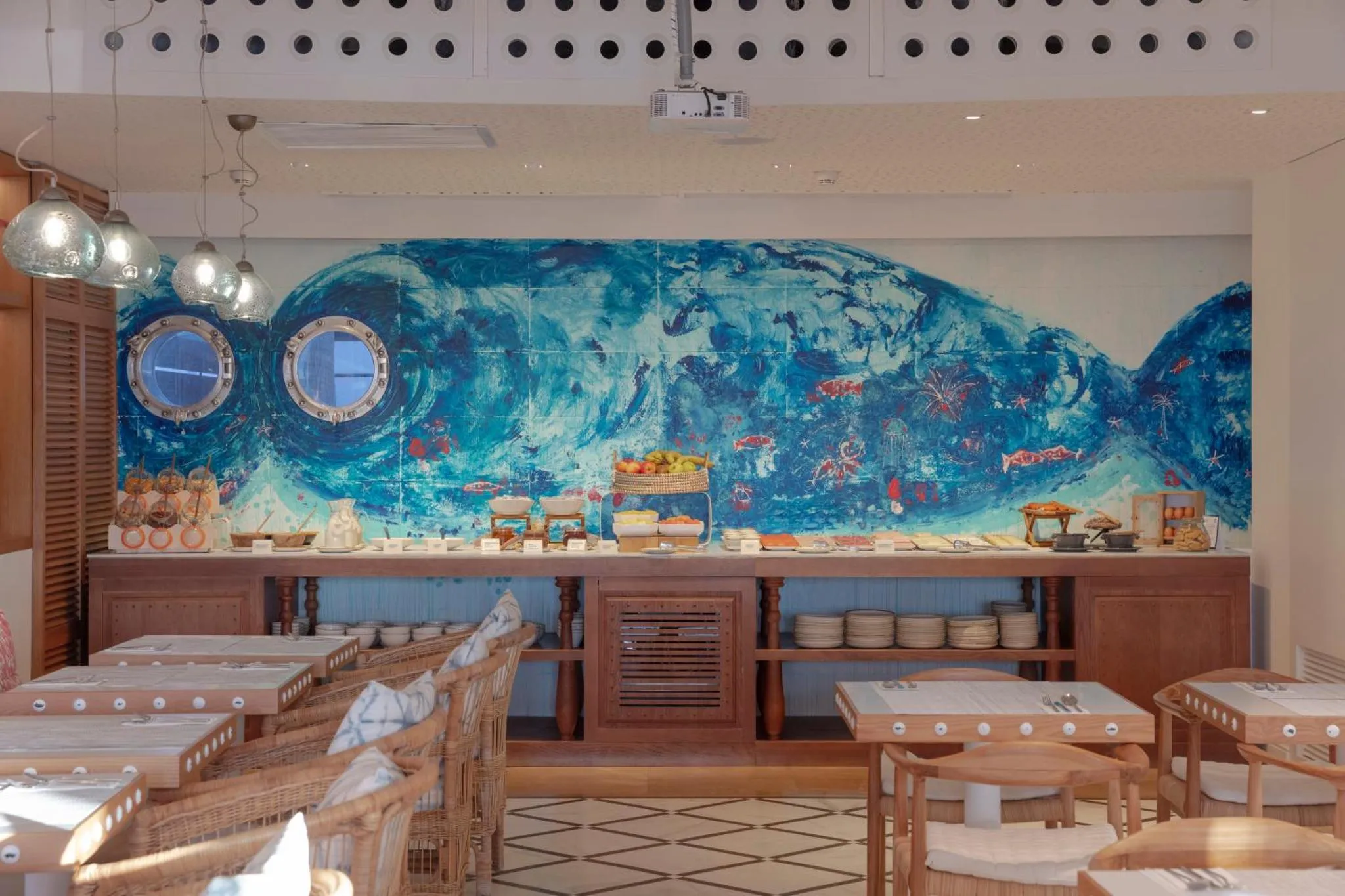 Une salle lumineuse avec des tables et un buffet décoré d'une fresque marine.