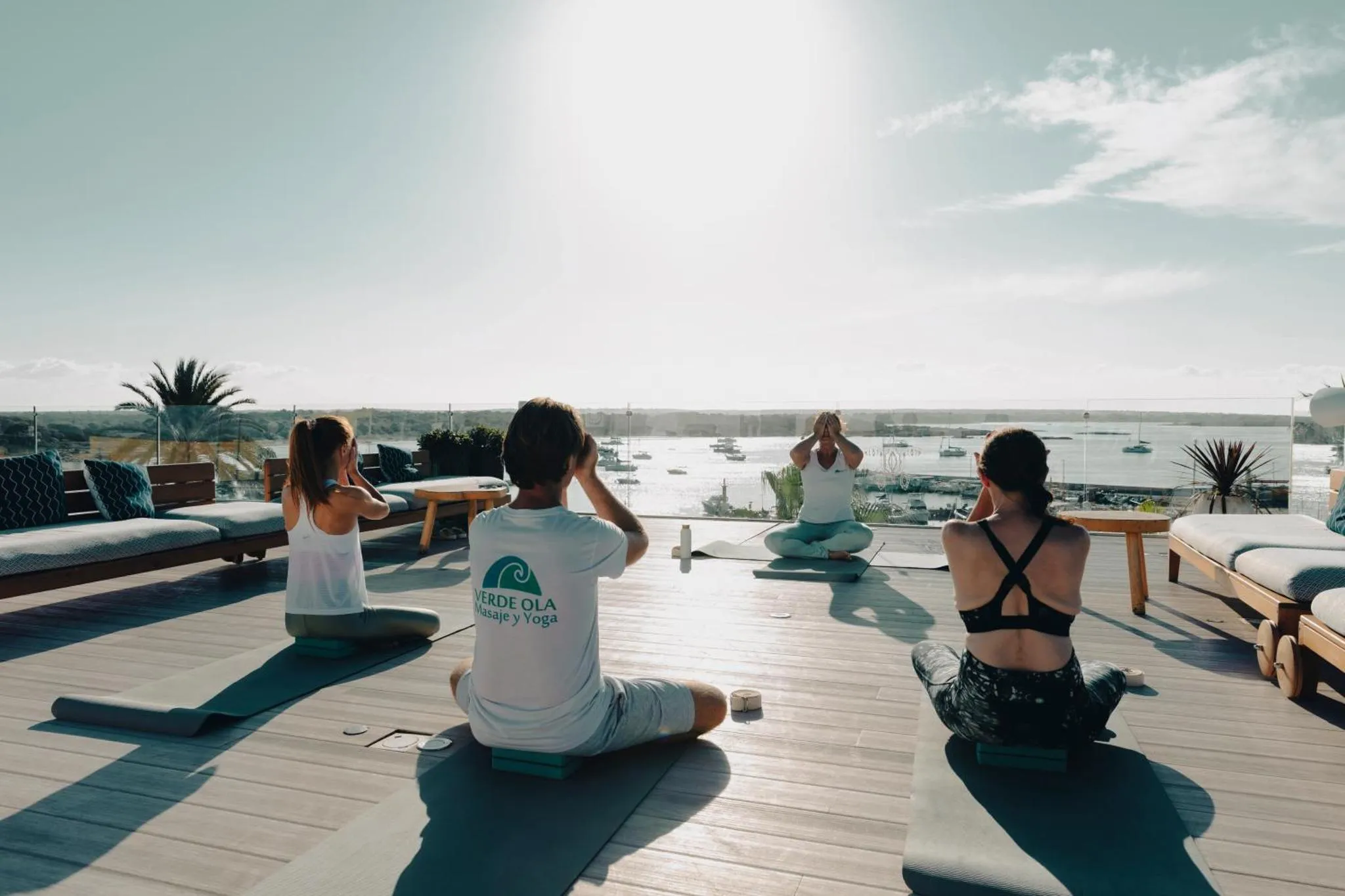 Des personnes pratiquent le yoga sur une terrasse en bois avec vue sur la mer.