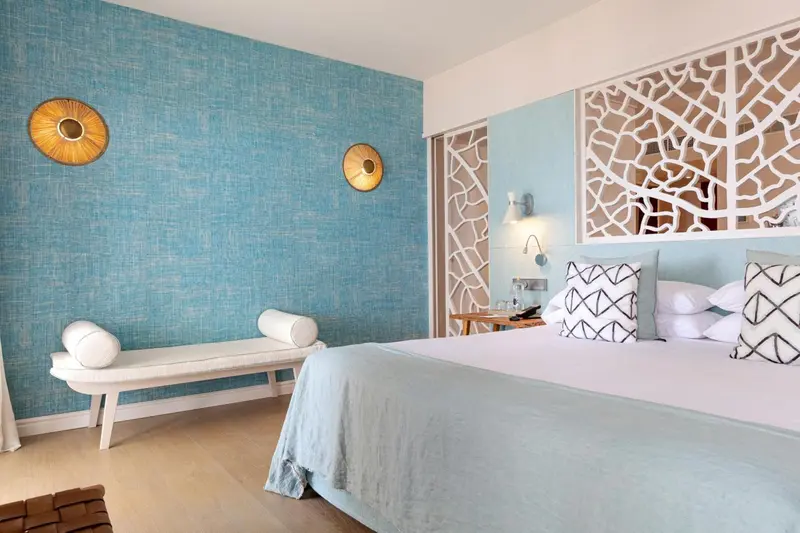 Une chambre lumineuse avec un lit décoré de coussins et un banc blanc.