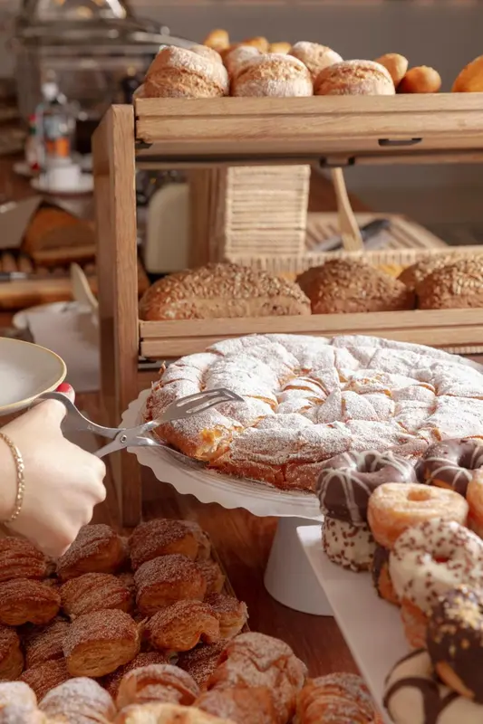 Une main sert une part de tarte sur un présentoir rempli de pâtisseries.