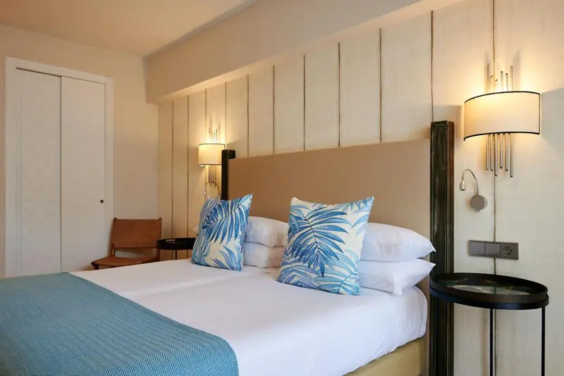 Une chambre lumineuse avec un grand lit recouvert d'une couverture turquoise et de coussins à motifs.