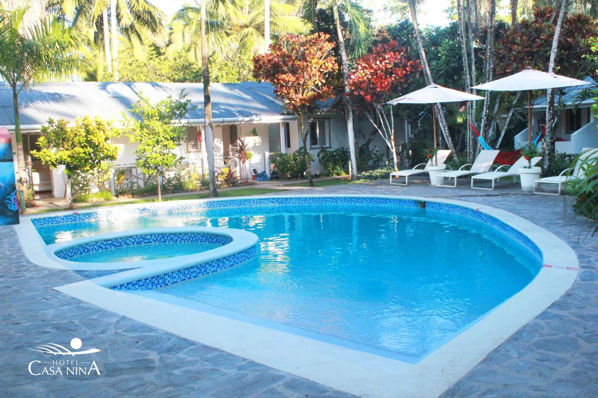 Piscine rectangulaire bordée d'une terrasse avec transats et végétation tropicale.