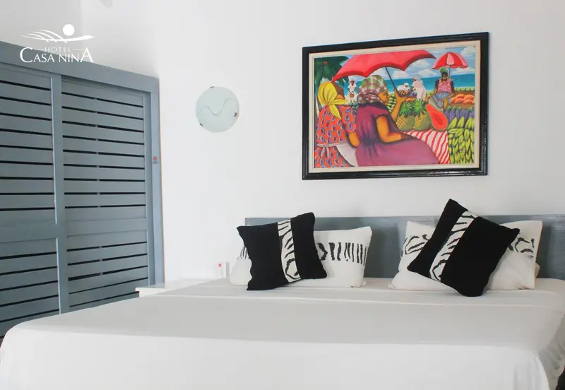 Une chambre lumineuse avec un lit recouvert d'oreillers décoratifs et une peinture colorée au mur.