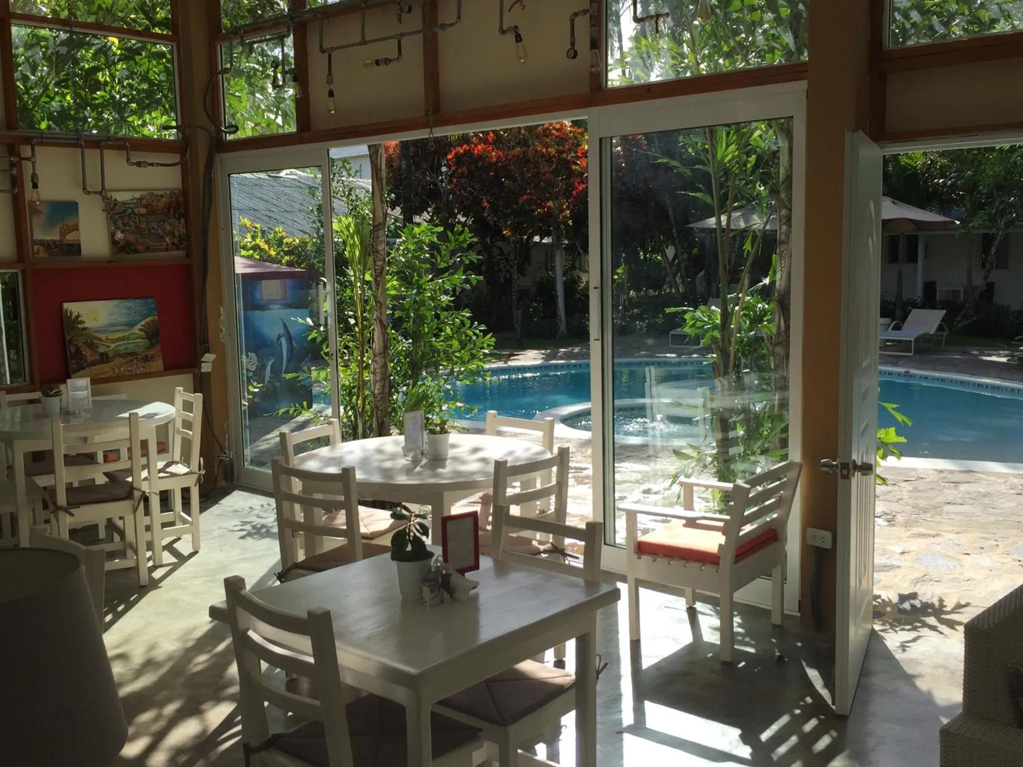 Une salle à manger lumineuse s'ouvre sur une piscine entourée de végétation.