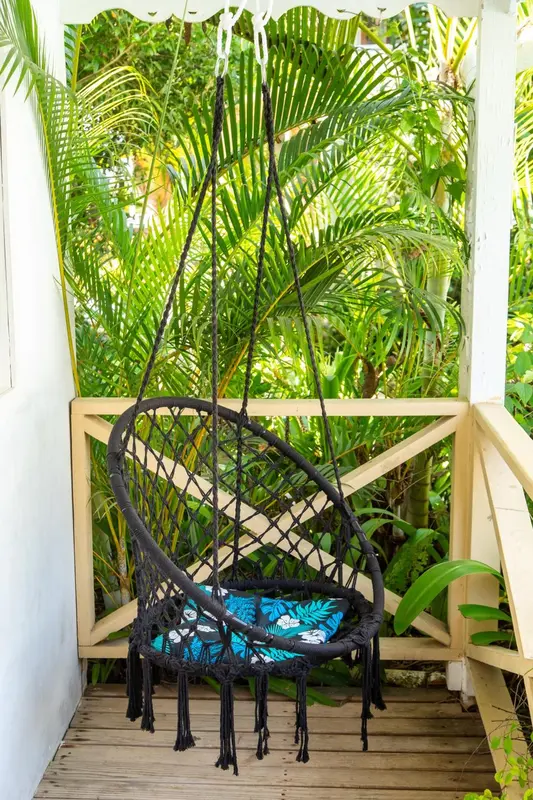 Un fauteuil suspendu en rotin se trouve sur une terrasse ombragée par la végétation.