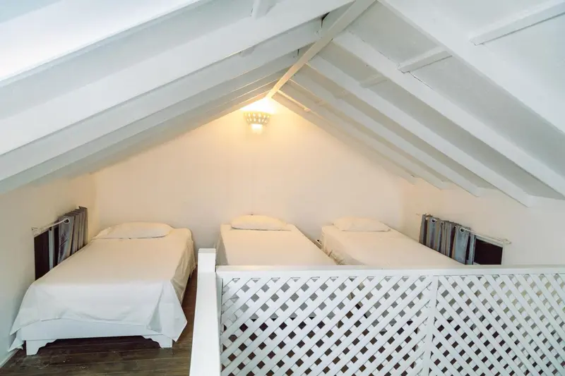 Une chambre mansardée avec trois lits simples et une rambarde en treillis.