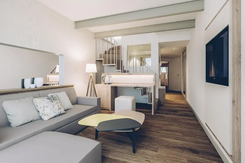Espace de vie intérieur lumineux avec canapé, table basse et escalier menant à une mezzanine.