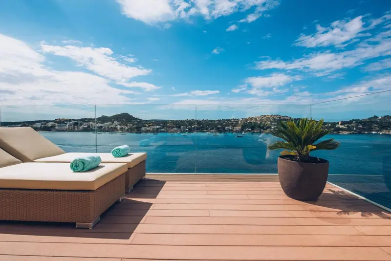 Deux transats avec des serviettes turquoise sur une terrasse en bois avec vue sur la mer et la côte.