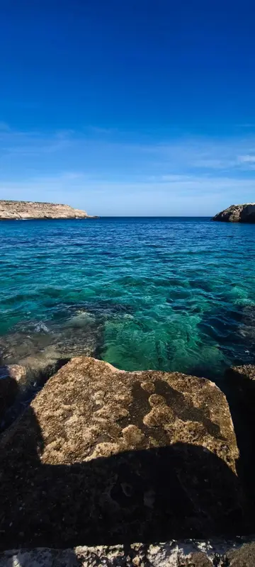 Cote rocheuse surplombant une mer turquoise sous un ciel bleu.