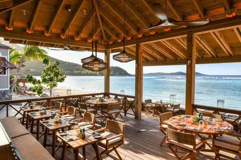 Terrasse ombragée avec tables et chaises donnant sur la mer.