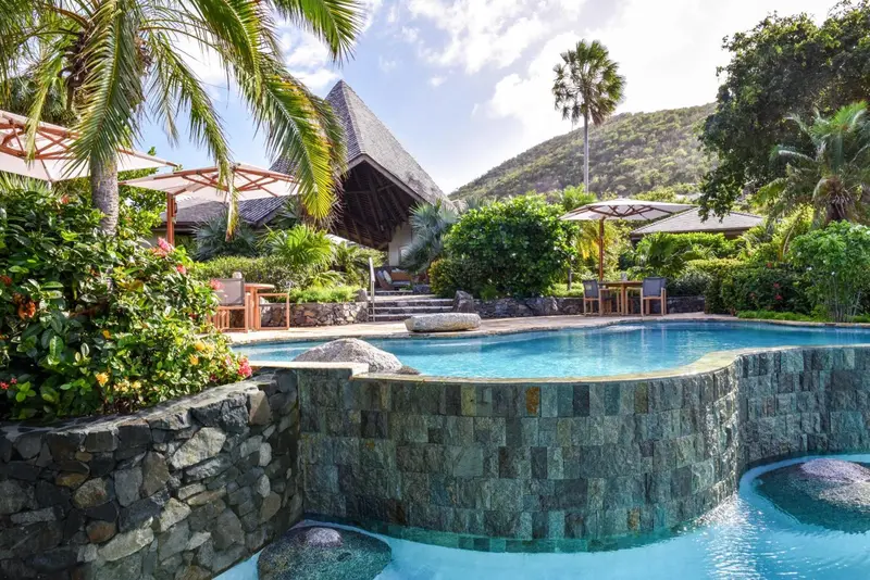 Piscine naturelle bordée de pierres et végétation tropicale.