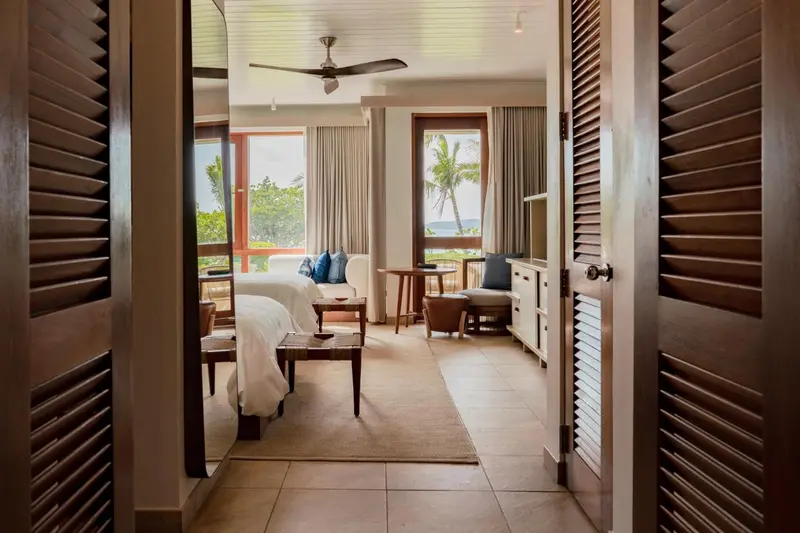 Une chambre lumineuse s'ouvre sur une vue sur la mer et la vegetation.