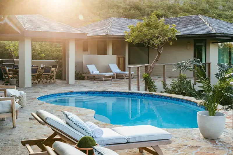 Une piscine bordée de chaises longues se trouve devant un bâtiment beige.