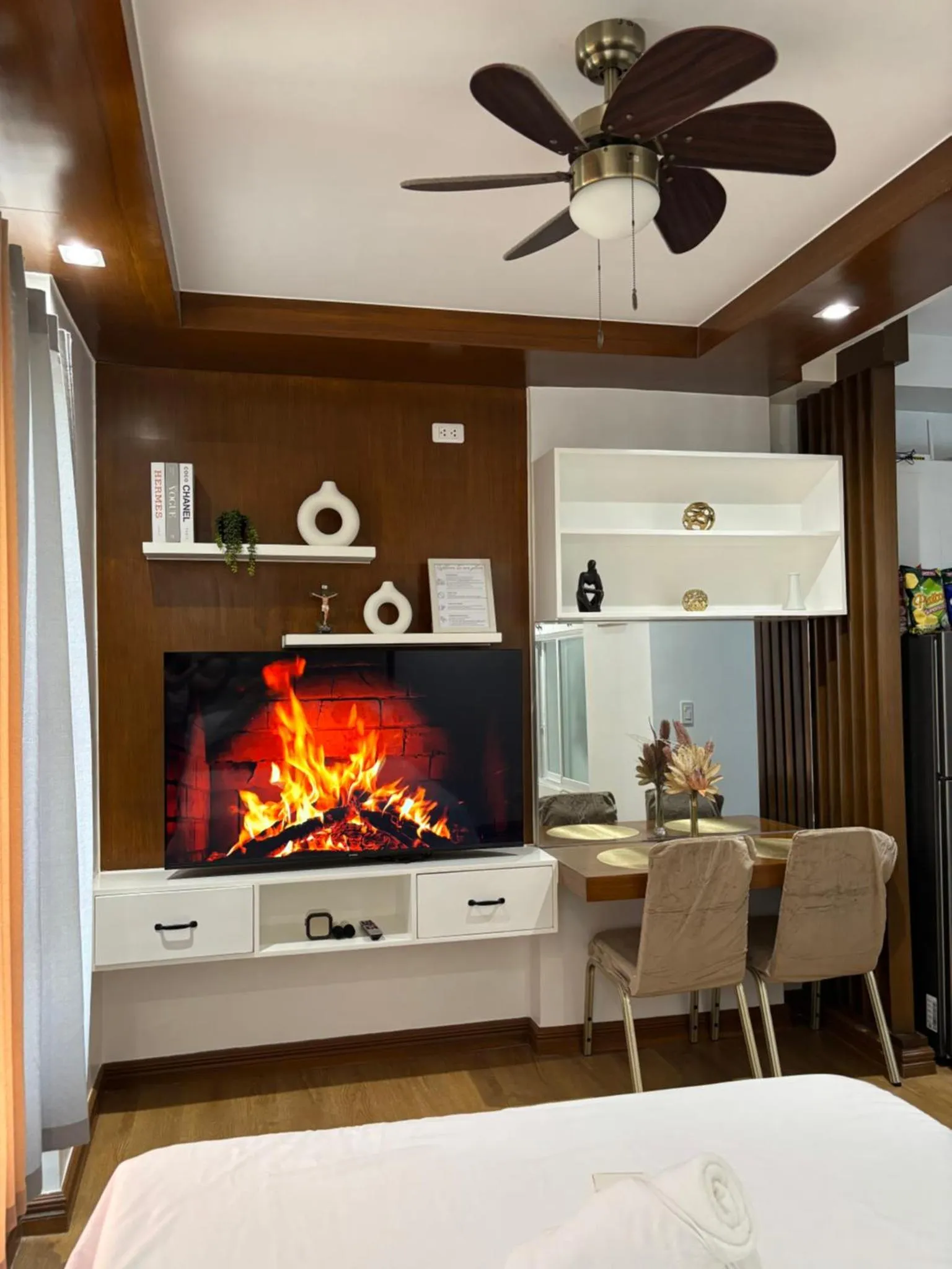 Une cheminée électrique illumine un espace de détente avec des fauteuils et des étagères décoratives.
