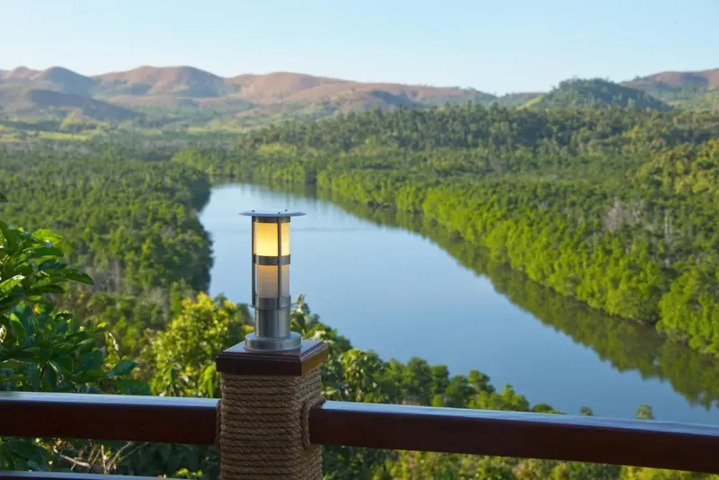 Vue panoramique sur une rivière et des collines verdoyantes depuis une terrasse.