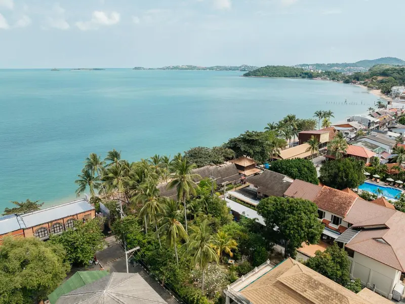 Vue aérienne d'une plage bordée de bâtiments et de végétation tropicale.