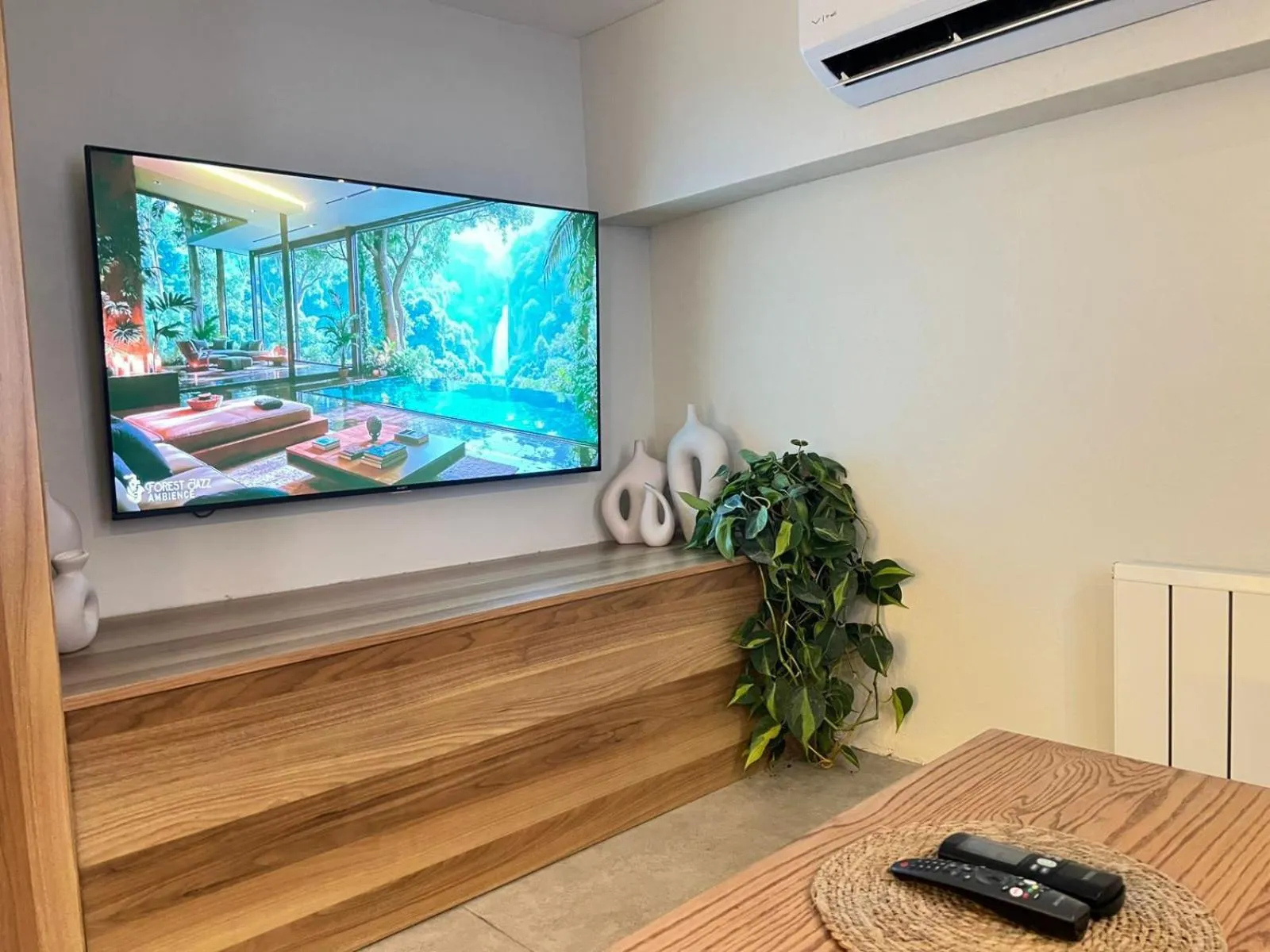 Une télévision murale diffuse une vue sur une piscine et une végétation luxuriante.
