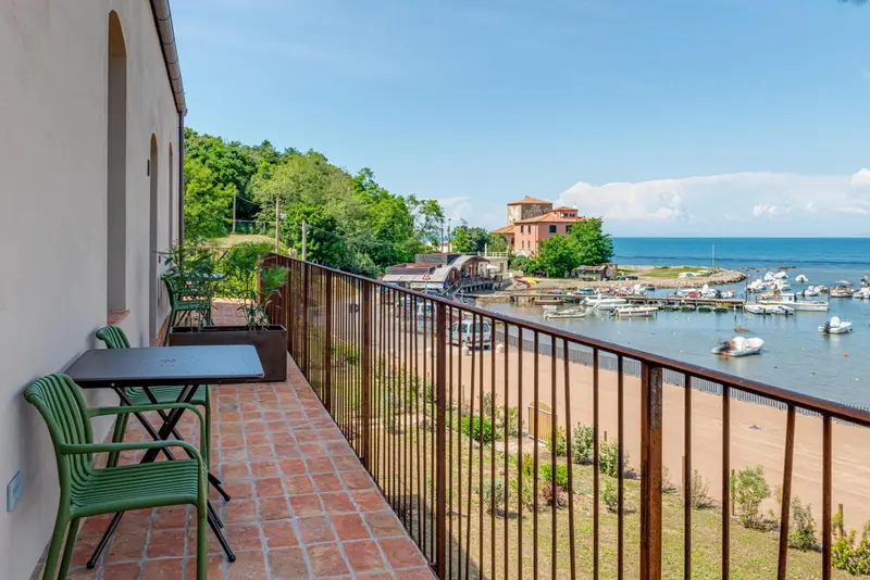 Terrasse avec mobilier vert donnant sur une plage et un port de plaisance.