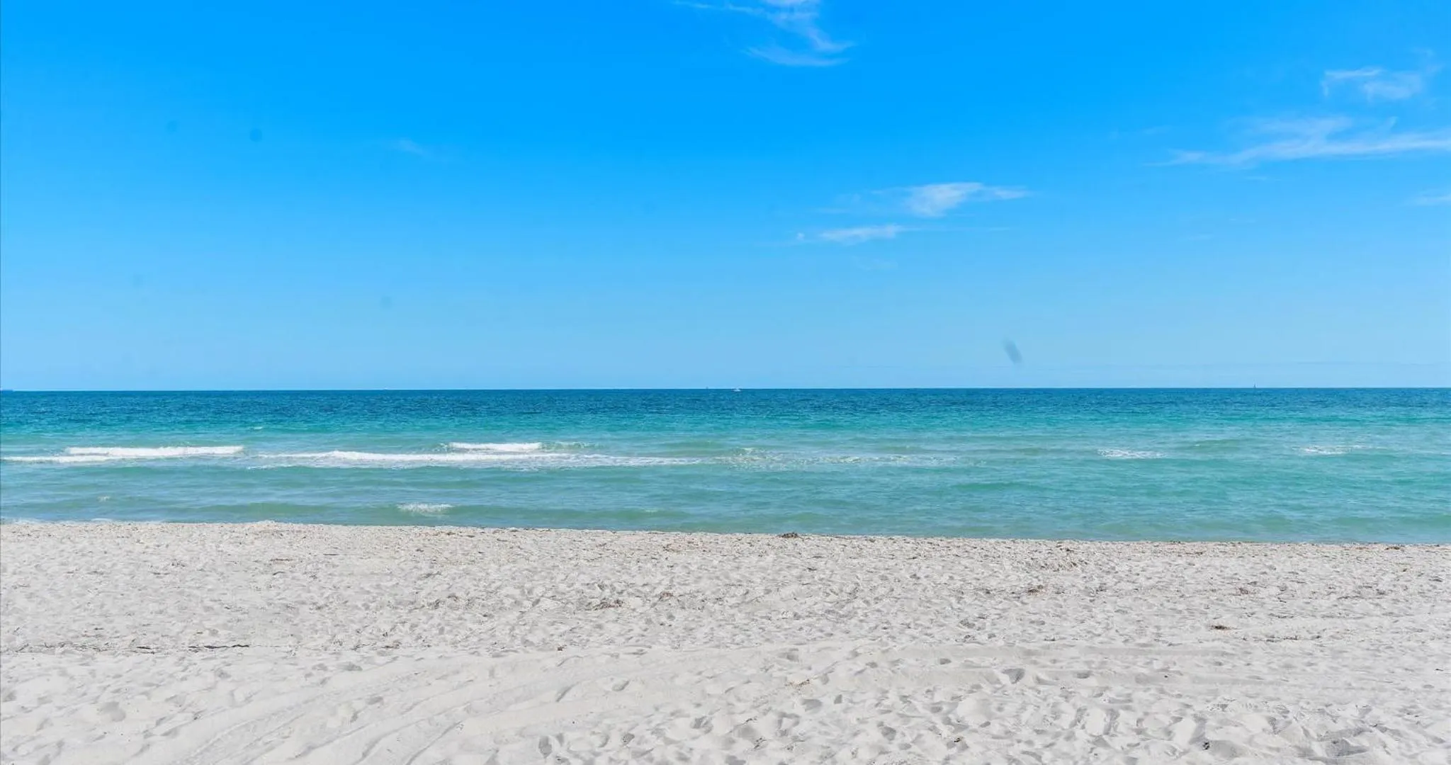Plage de sable fin bordée par une mer turquoise sous un ciel bleu.