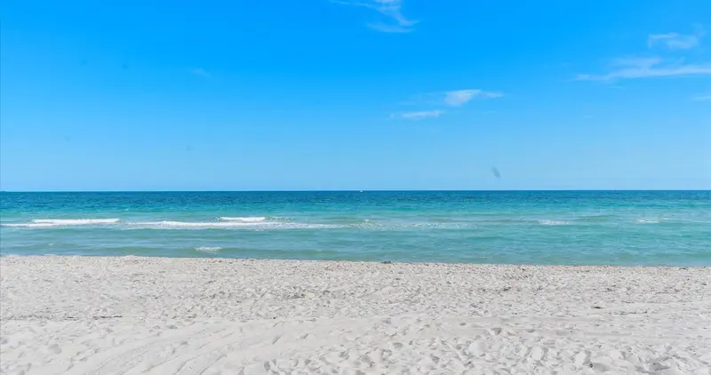 Plage de sable fin bordée par une mer turquoise sous un ciel bleu.