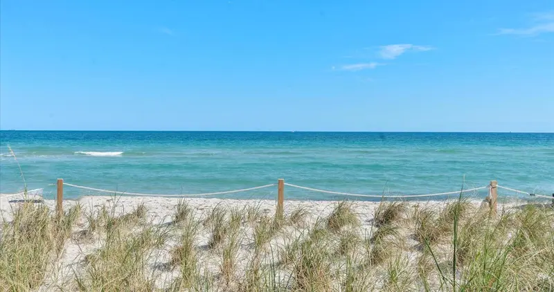 Plage de sable avec herbes et mer turquoise sous un ciel bleu.