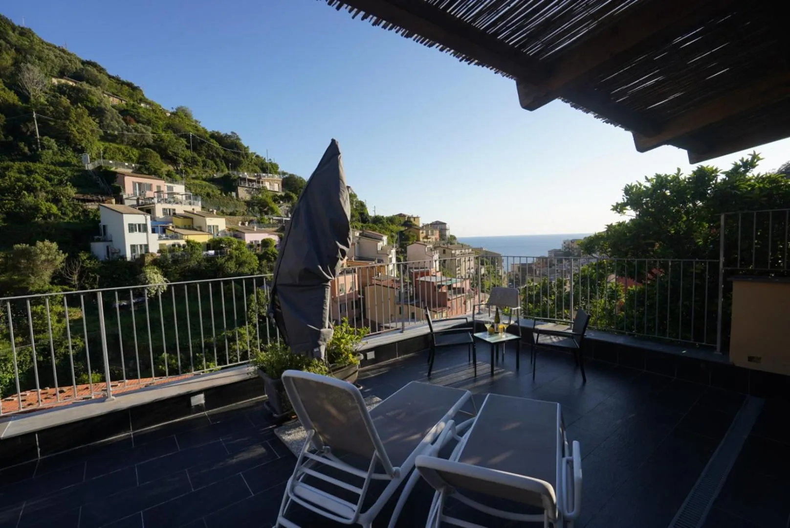 Terrasse ombragée avec mobilier de jardin et vue sur la mer et les collines.