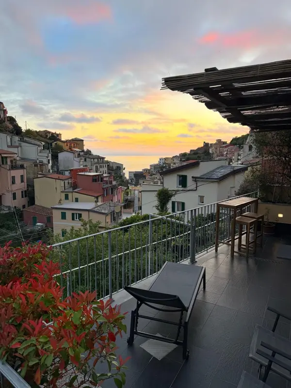 Terrasse avec mobilier d'extérieur donnant sur un village et la mer au coucher du soleil.