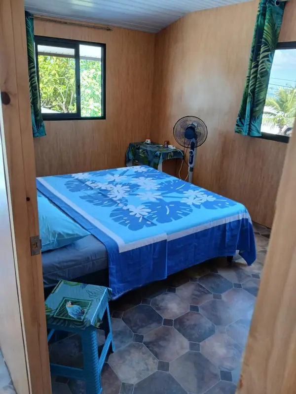 Une chambre simple avec un lit recouvert d'une couverture bleue et une fenêtre donnant sur la végétation.