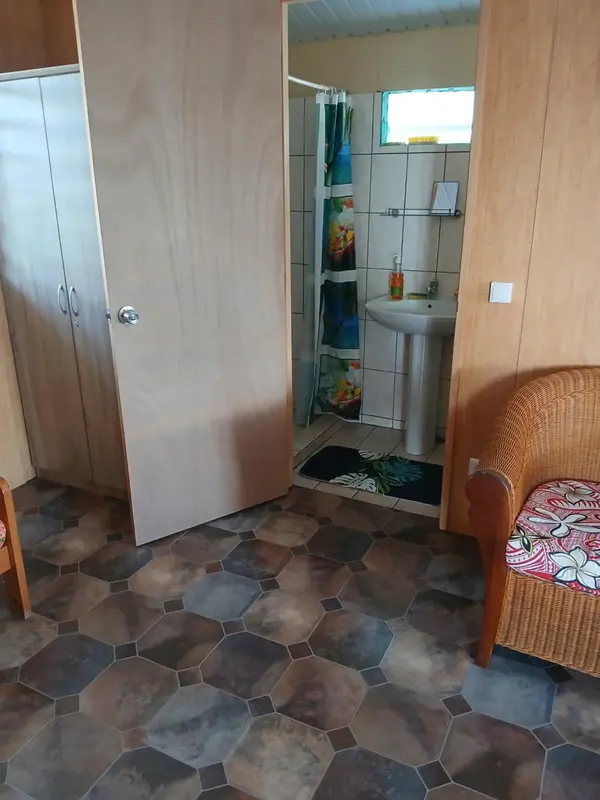 Une porte ouverte donne sur une salle de bain carrelée avec un lavabo et une douche.