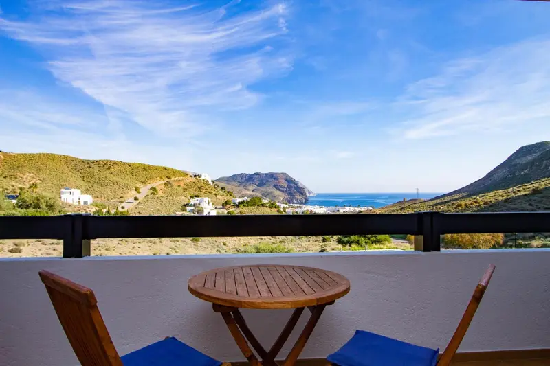 Terrasse avec mobilier en bois donnant sur une vue côtière ensoleillée.