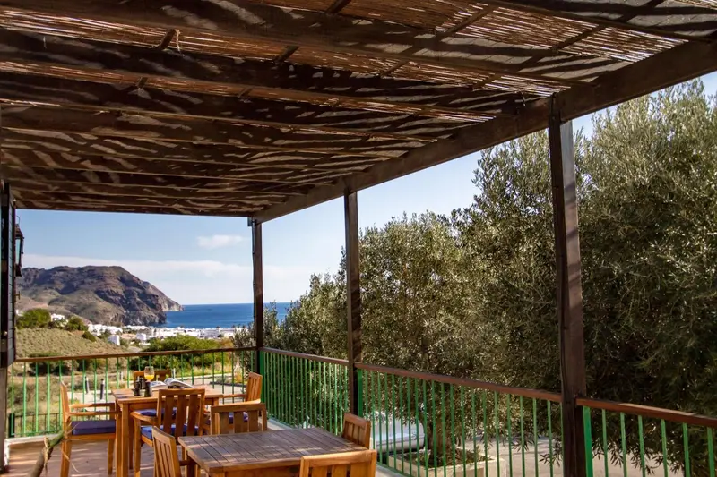 Terrasse ombragée avec tables et chaises donnant sur un paysage côtier.