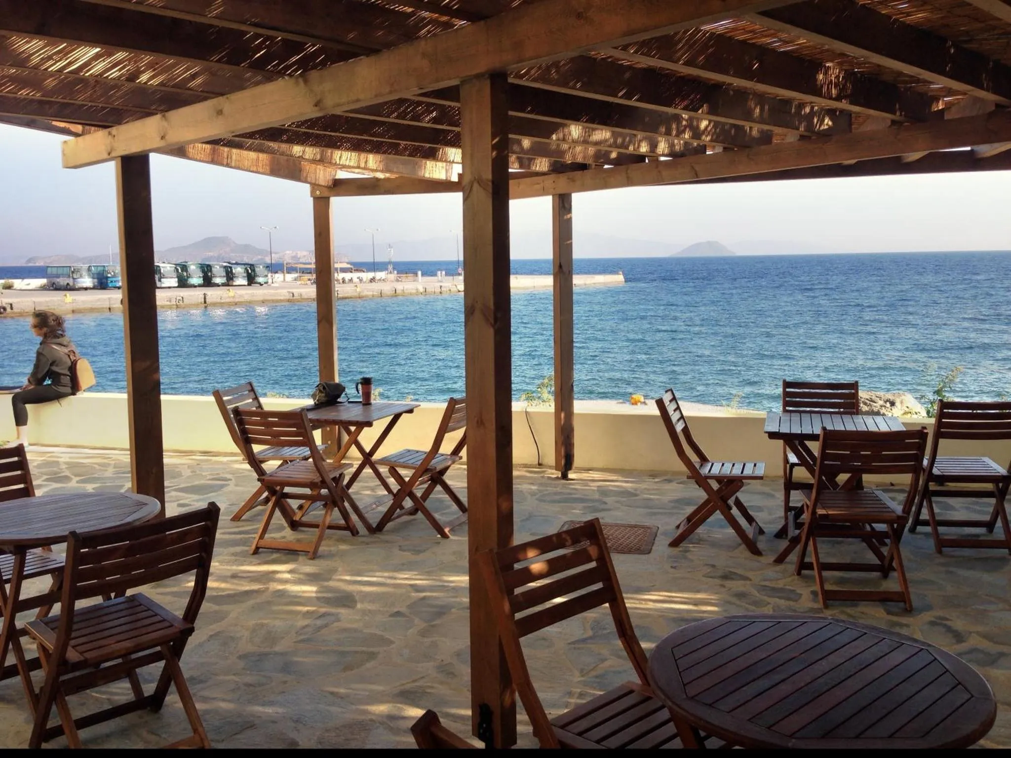 Terrasse ombragée avec tables et chaises donnant sur la mer.
