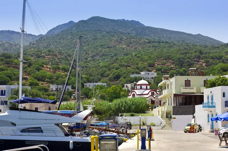 Vue d'un port de plaisance avec des bateaux et des bâtiments blancs sur une colline verdoyante.