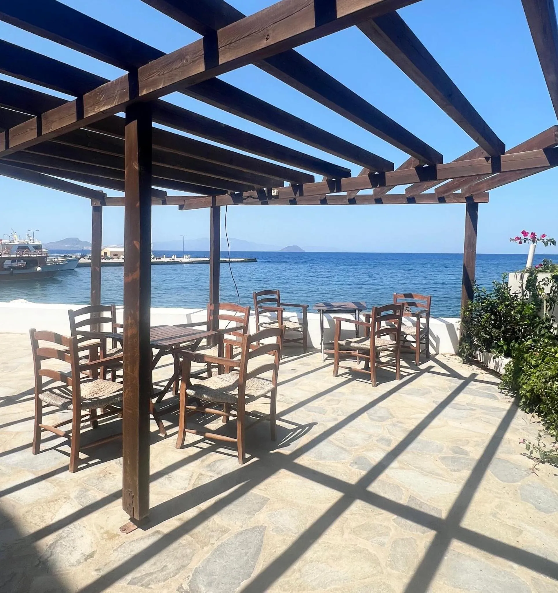 Terrasse ombragée avec tables et chaises donnant sur la mer.