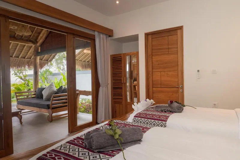 Une chambre lumineuse avec un lit décoré et un coin salon ouvert sur l'extérieur.