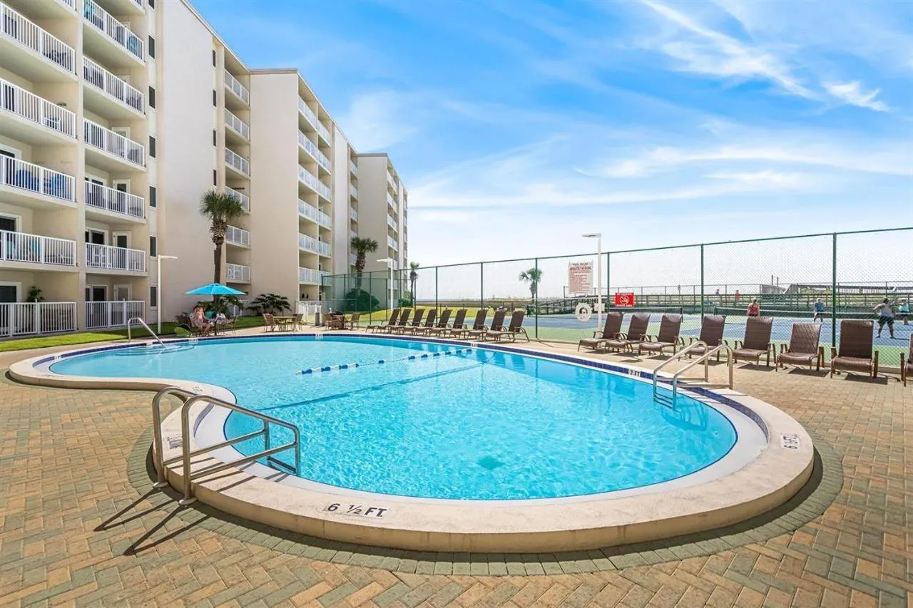 Une piscine rectangulaire entourée d'une terrasse pavée avec des transats et des parasols.
