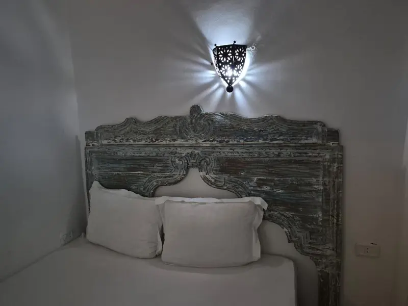 Un lit avec une tête de lit sculptée est éclairé par une applique murale.