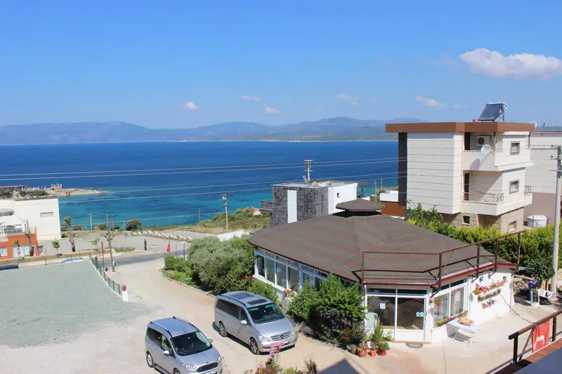 Vue aérienne d'un bâtiment avec des véhicules garés devant et la mer en arrière-plan.