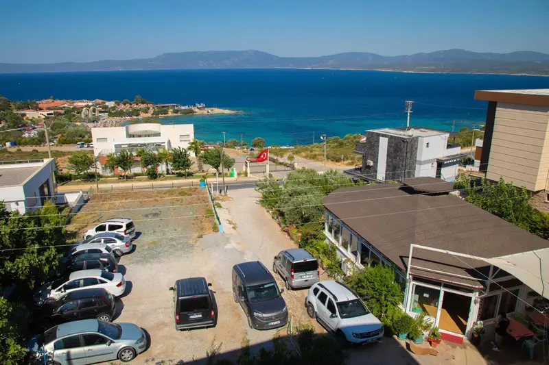 Vue aérienne d'un parking devant des bâtiments blancs et bruns, avec la mer en arrière-plan.