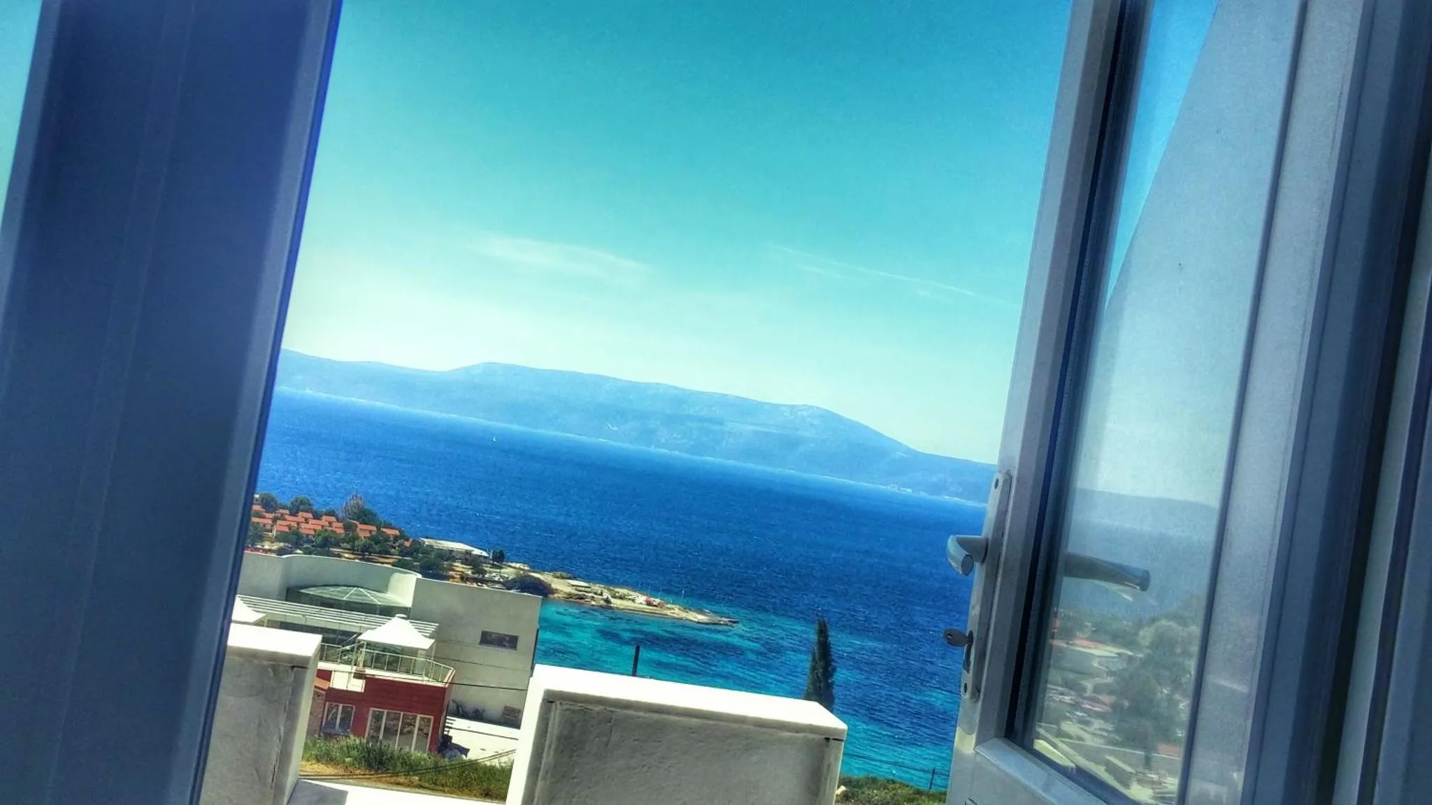 Vue sur la mer et les montagnes depuis une fenêtre ouverte.