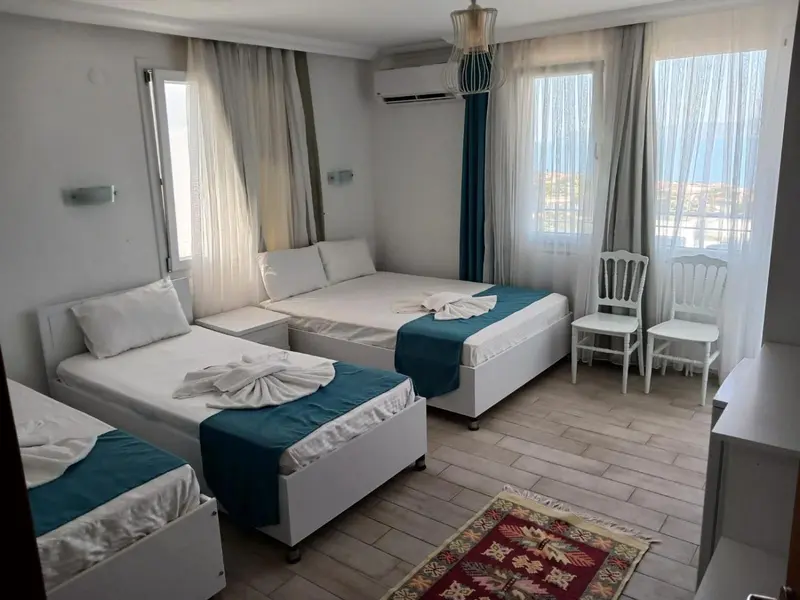 Chambre avec deux lits simples et un lit double, décorée de rideaux turquoise.