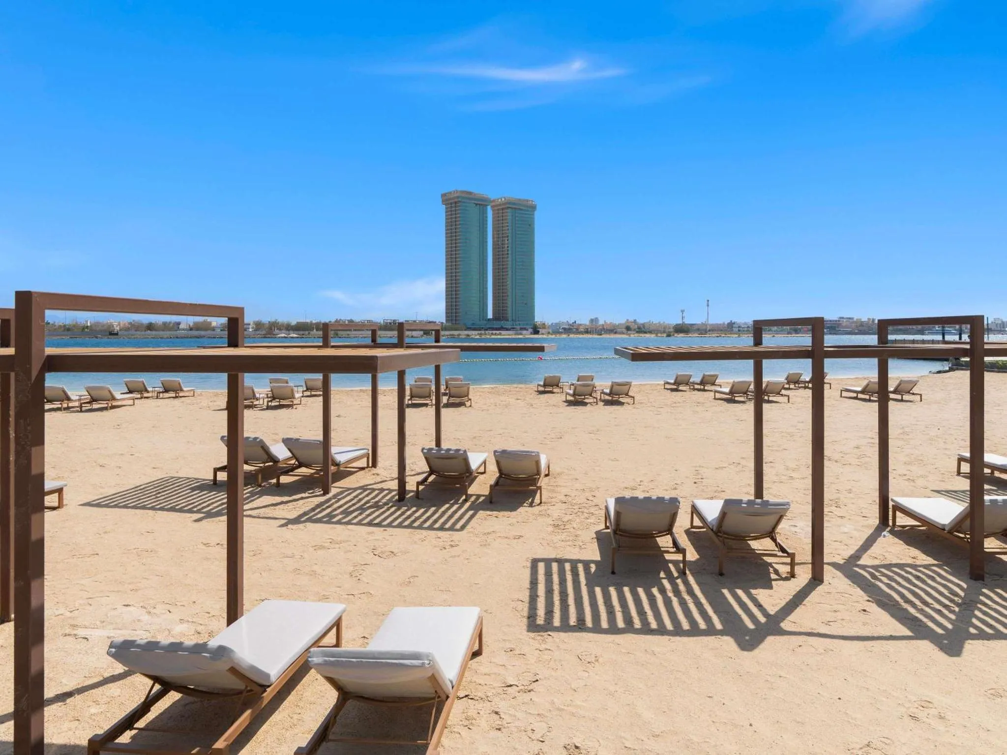 Transats alignés sur une plage de sable fin, abrités par des structures en bois.