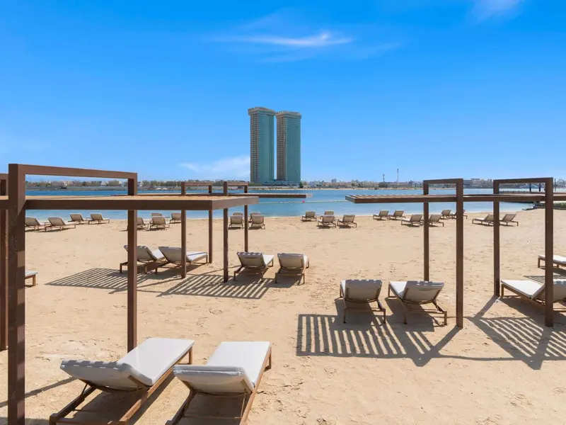 Transats alignés sur une plage de sable fin, abrités par des structures en bois.