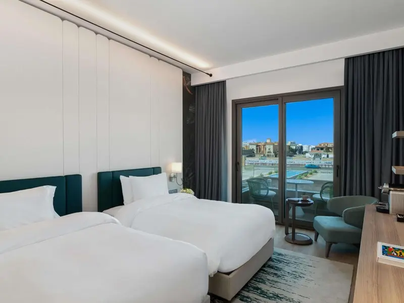 Chambre lumineuse avec deux lits simples et vue sur une piscine.